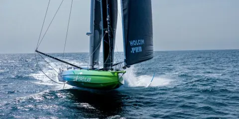 Voilier vert et bleu "Go Circular" naviguant à pleine vitesse, voiles noires marquées "Holcim PRB". Un design de Guillaume Verdier.