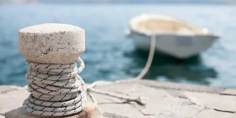 Un cordage est enroulé autour d'une borne en pierre sur un quai, prêt pour le prochain pendille bateau.