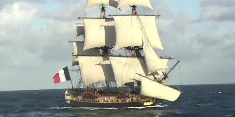 La frégate Hermione, fierté de la marine française, navigue majestueusement sur l'océan, ses voiles gonflées par le vent.