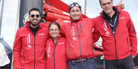 Erwan Thiboumery et trois autres personnes souriantes portent des vestes rouges du Groupe Interaction, devant un bateau.