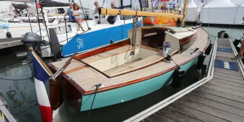 Un élégant belouga bateau, aux finitions bois et coque turquoise, est amarré à quai.