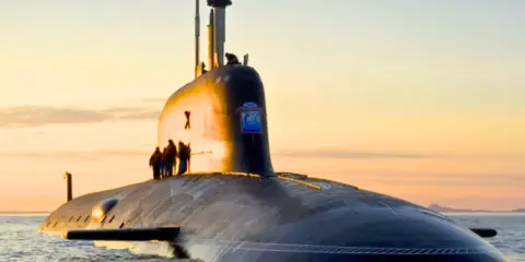 Un imposant sous-marin, potentiellement le sous-marin le plus puissant du monde, navigue sur une mer calme au coucher du soleil.