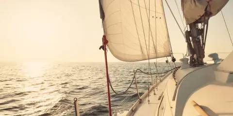 Voile de bateau gonflée par le vent, naviguant sur une mer calme au coucher du soleil.