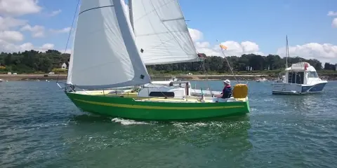 Un voilier vert vif navigue sur l'eau, avec un autre bateau à moteur en arrière-plan. Une belle journée pour une croisière, peut-être avec une dégustation d'armagnac à bord de ce bateau.