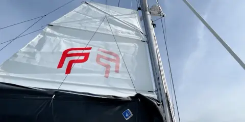 Voile blanche avec logo rouge, prête à naviguer à la voile sous un ciel bleu.