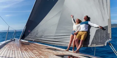 Un couple heureux profite du soleil sur un voilier. Ils semblent avoir fait le bon choix en décidant de choisir un voilier pour leurs vacances.