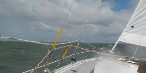 Vue depuis un voilier, mer agitée sous un ciel nuageux. Le gréement et la voile blanche sont visibles. Fiche technique du Challenger Scout.