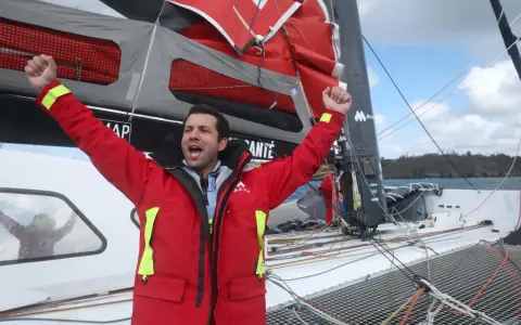 Un marinier en veste rouge célèbre sur un voilier. Une opportunité unique : ce voilier est à donner gratuitement !