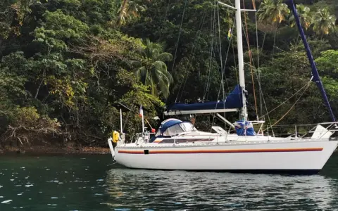 Voilier blanc ancré près d'une côte luxuriante et verdoyante. Le trismus 32 semble prêt pour une aventure tropicale.