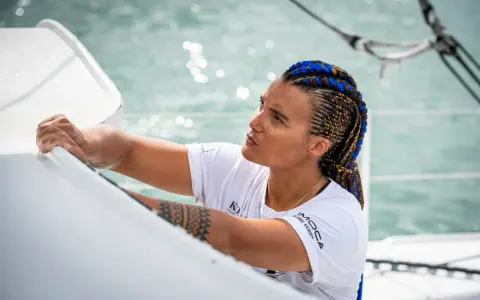 Marie Tabarly, concentrée, ajuste une voile sur son bateau. Ses tresses bleues et brunes flottent au vent.