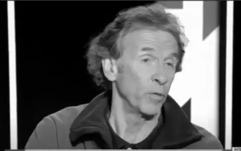 Portrait en noir et blanc d'Éric Loizeau, homme aux cheveux ondulés, parlant dans un micro.