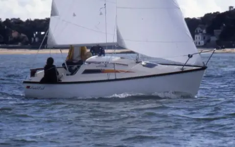 Voilier blanc naviguant sur une mer agitée, avec deux personnes à bord. Les premiers 18 avis sur ce modèle de bateau sont positifs.