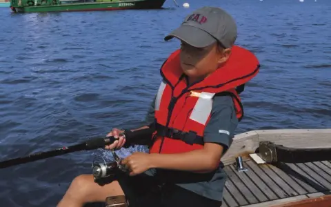 Un enfant pêche en mer, portant un gilet de sauvetage obligatoire. La question du gilet de sauvetage obligatoire jusqu'à quel âge est cruciale pour la sécurité nautique.