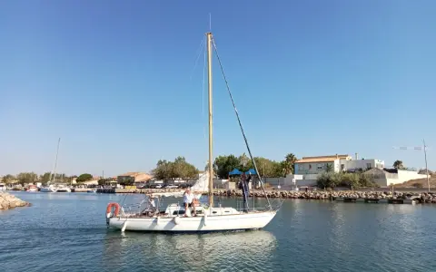 Un voilier atlante navigue sur des eaux calmes, avec des personnes à bord. Le ciel est bleu et dégagé.