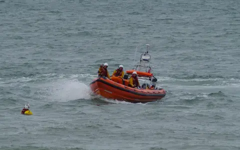 Bateau de sauvetage orange avec équipage en action. Une personne dans l'eau, une fusée de détresse bateau obligatoire est essentielle.