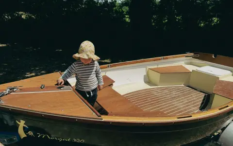 Un enfant en chapeau fleuri explore l'intérieur d'un bateau en bois, le Morgat 320, prêt pour l'aventure.