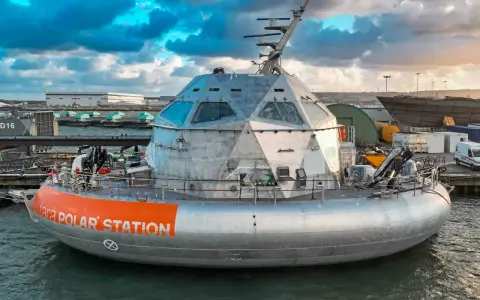 Le bateau Tara Polar Station, une station polaire futuriste, est amarré dans un port sous un ciel dramatique.