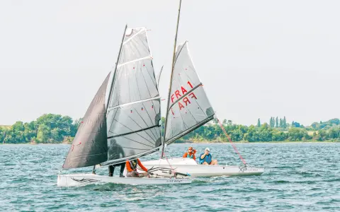 Deux voiliers d'aviron modernes naviguent sur un lac, avec des équipages concentrés sur la course.