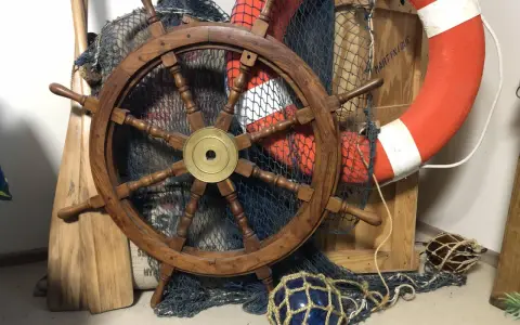 Roue de gouvernail en bois, filet de pêche, bouée de sauvetage orange et pagaies évoquent un safran de bateau prêt pour l'aventure.
