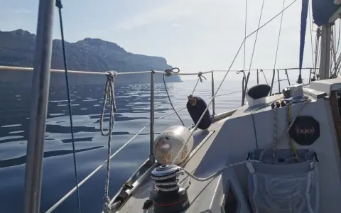 Vue depuis un voilier Aquila, naviguant sur une mer calme avec des falaises en arrière-plan. Avis de navigation paisible.