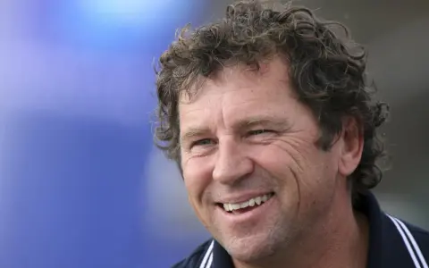 Lionel Lemonchois, skipper souriant, cheveux bouclés, sur fond bleu.
