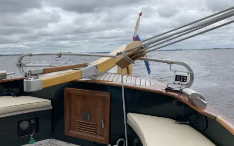 Installation pilote automatique barre franche sur un voilier, avec drapeau néerlandais et ciel couvert.