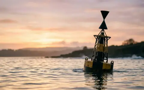 Une bouée jaune et noire, un bms bateau, flotte sur l'eau calme au coucher du soleil.