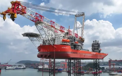 Le bateau grue "Wind Ally" est prêt à installer une éolienne en mer. Sa structure imposante domine le port.