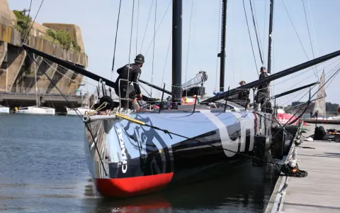 L'IMOCA Charal, un voilier de course futuriste, est amarré à quai. Des marins s'affairent sur le pont, préparant le navire pour une nouvelle aventure en mer.