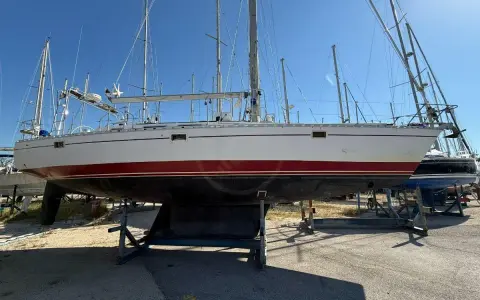 Un voilier blanc et rouge, prêt pour l'aventure, est exposé sur des bers. Ce navire, un modèle de **Gibert Marine**, attend de retrouver les flots.