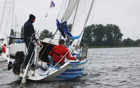 Deux hommes naviguent sur un voilier micro challenger, le vent gonflant les voiles sur un lac calme.