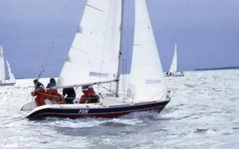 Un voilier nommé "FUN" navigue sur une mer agitée, avec des personnes à bord profitant de la navigation.