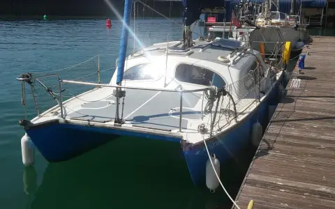 Un catamaran Hirondelle bleu et blanc, amarré à un ponton en bois, prêt pour une nouvelle aventure sur l'eau.