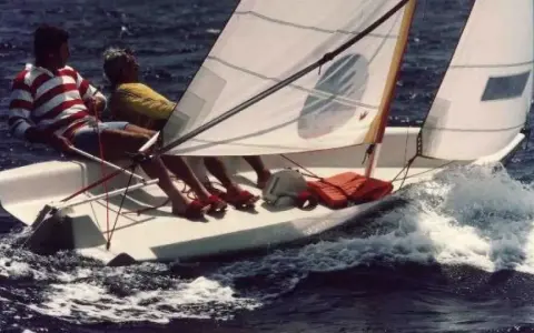 Deux personnes naviguent sur un dériveur Wizz, le bateau fend les vagues dans une joyeuse course.