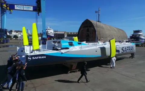 Équipe poussant un **60 pieds IMOCA** de course au large, le Safran, dans un chantier naval.