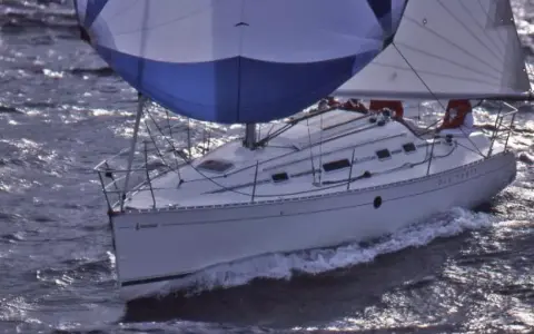 Voilier blanc naviguant sur des eaux agitées, ses voiles bleues et blanches gonflées par le vent. Le nom "DIE-TERRY" est visible sur la coque.