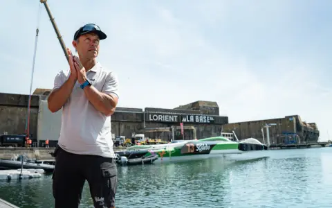 Un homme applaudit devant le trimaran Sodebo Ultim 4, prêt à naviguer.
