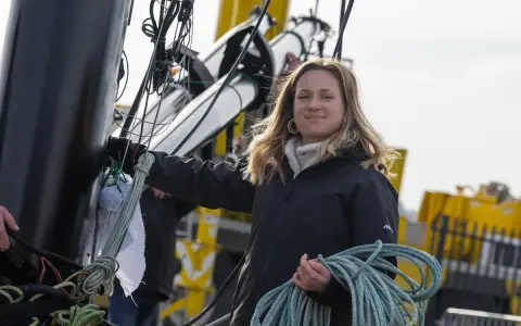 Élodie Bonafous, souriante, tient une corde bleue sur un bateau, entourée de cordages et de structures métalliques.