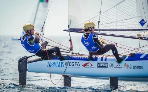 Deux jeunes navigateurs, dont Lou Berthomieu, en action sur un catamaran de sport, le vent gonflant les voiles.