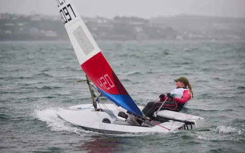 Jeune navigatrice en dériveur **tabur 320**, voile rouge et bleue, naviguant sur une mer agitée.