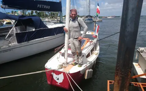 Yann Quenet, prêt pour l'aventure avec son baluchon, pose sur son voilier orné d'une poule.