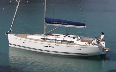 Un voilier blanc Dufour 405 Grand Large navigue sur une eau turquoise. Un homme est au poste de barre.