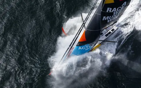 Le voilier de Boris Herrmann fend les vagues, projetant une gerbe d'eau. La voile arbore "Race we must win".