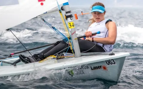 Jeune femme concentrée naviguant en deriveur solo, le bateau #063 fend les vagues.