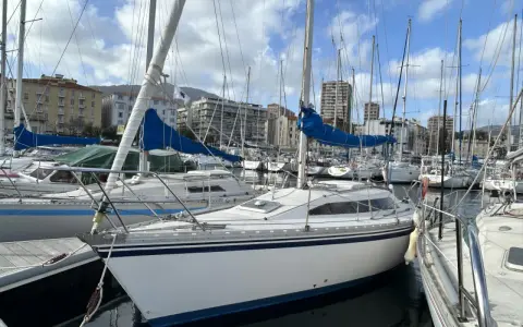 Un voilier blanc aux voiles bleues, amarré dans un port. L'avis sur ce voilier rush est qu'il est prêt pour la prochaine aventure.