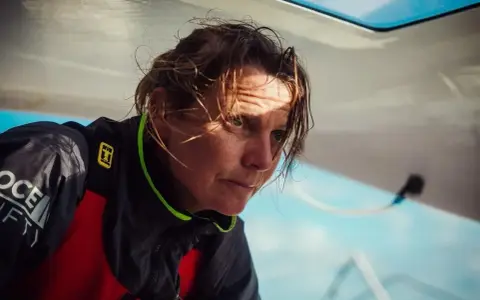 Anne Claire Le Berre, concentrée, le regard intense, le visage marqué par le soleil et le vent, sur un bateau.