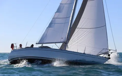 Un voilier Jeanneau Symphony navigue sur une mer agitée, ses voiles blanches gonflées par le vent. Un avis positif pour ce bateau.