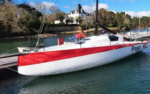 Le voilier Pogo RC, blanc et rouge, est amarré à un ponton. Une personne en blouson rouge est à bord.