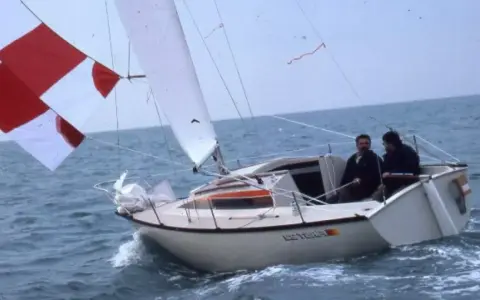 Deux hommes naviguent sur un voilier blanc, le "Esterel", avec des voiles rouges et blanches. Les premiers 22 avis sur ce bateau sont probablement très positifs.