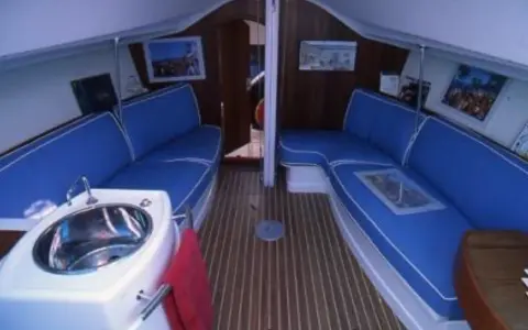 Intérieur du JOD 35, avec banquettes bleues, évier en inox et parquet en bois. Prêt pour une nouvelle aventure en mer.